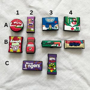 Può includere: Un set di 12 ciondoli colorati in stile cartone animato che rappresentano marchi britannici popolari di cibo e bevande. I ciondoli includono formaggio Babybel, tè Tetley, tè PG Tips, caramelle Squashies, caffè Nescafé, noodles Popperami, cioccolato Milkybar e cioccolato Dairy Milk Freddo.