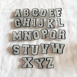 May include: A set of 26 silver glitter letters, each with a black outline, spelling out the alphabet from A to Z. The letters are arranged in three rows.