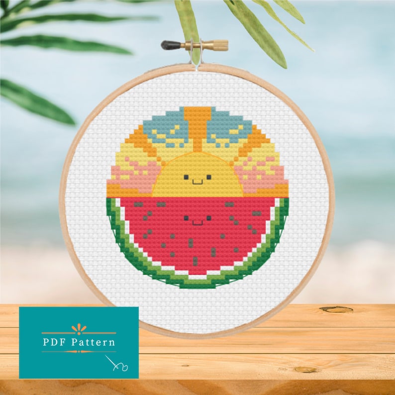 Embroidery hoop with a kawaii style slice of watermelon smiling just below a kawaii style sunset also smiling. The watermelon and sunset are joined to form a circle and are stitched in cross stitch using bright summery colours.
