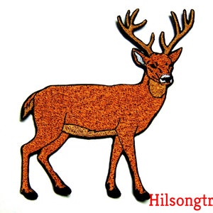 May include: A brown embroidered patch of a deer with antlers. The deer is standing on all four legs and facing to the right. The patch is made of a soft, fuzzy material.