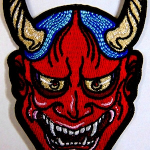 May include: Red and blue embroidered Japanese Oni mask with horns. The mask has a fierce expression with sharp teeth and large eyes.