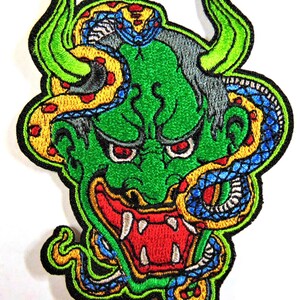 May include: Embroidered patch featuring a green oni demon with red eyes and a large open mouth. A yellow and blue snake is wrapped around the demon's head and body.