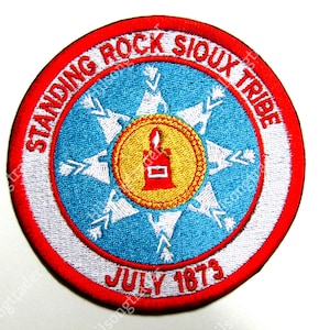 May include: A red, white, and blue embroidered patch with the text "Standing Rock Sioux Tribe" and "July 1873". The patch features a stylized star with a flame inside.