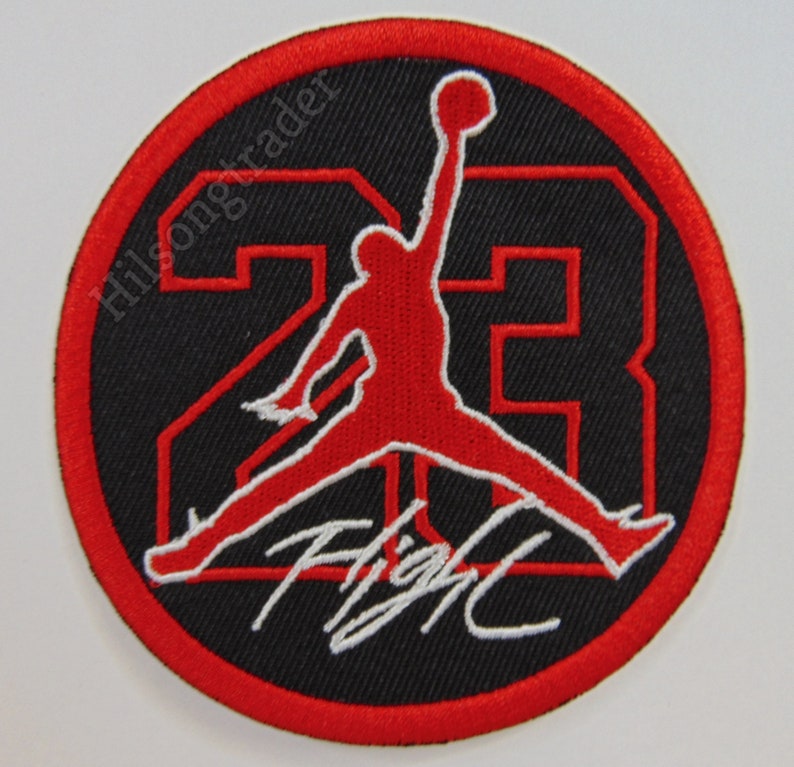 Round, iron-on patch with red border, black fabric, and red Jumpman Jordan in the middle. Outlined "23" behind the Jumpman with the scripted word "Flight" on the bottom of the patch.