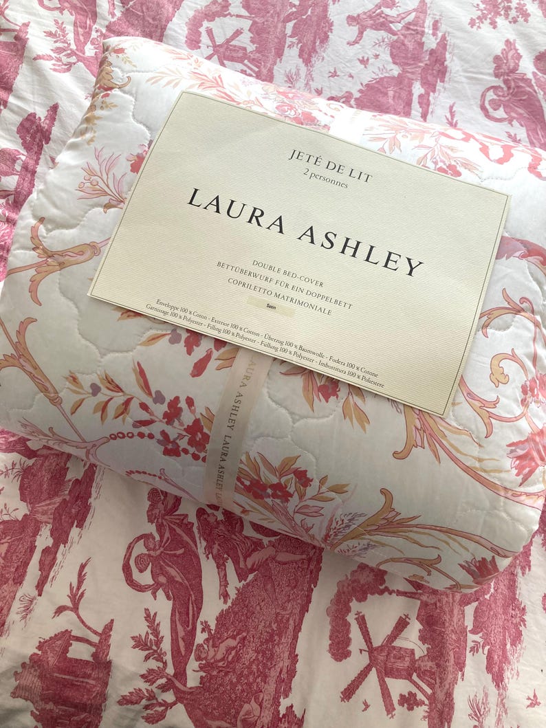 May include: A double bed cover by Laura Ashley, featuring a floral and pastoral design in shades of pink and cream. The cover is quilted and includes the text "JET&Eacute; DE LIT" and "DOUBLE BED COVER".