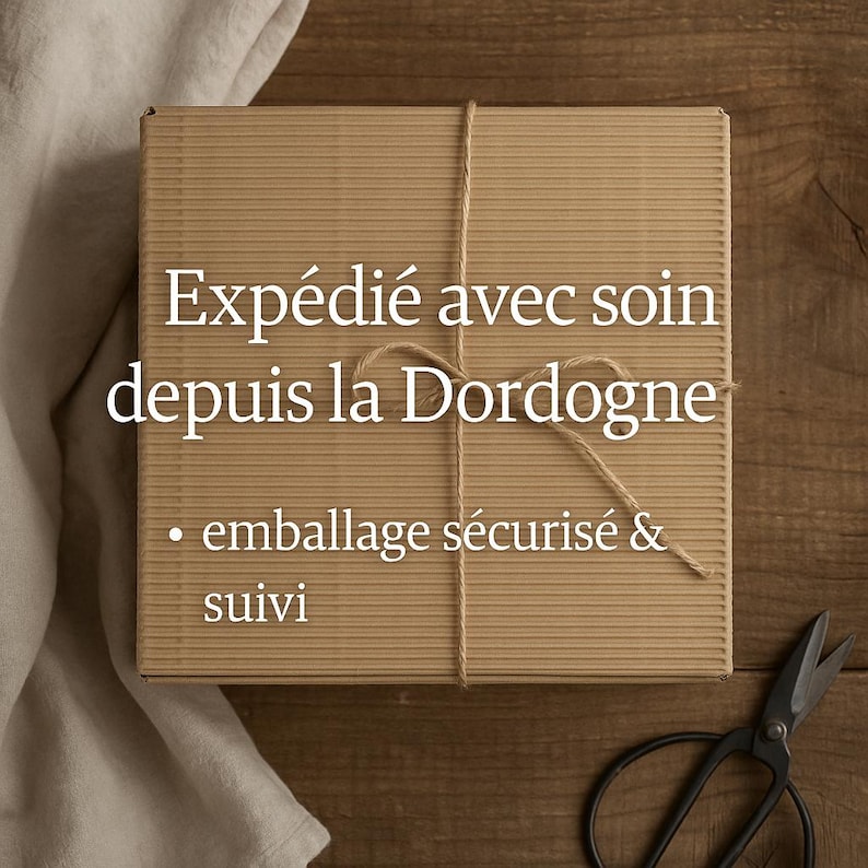May include: A brown cardboard box tied with twine, with text in white. The box is on a wooden surface, with a pair of scissors in the lower right corner. The text on the box reads: "Exp&eacute;di&eacute; avec soin depuis la Dordogne" and "emballage s&eacute;curis&eacute; & suivi."