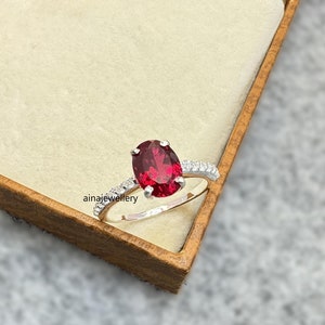 May include: A silver ring with a large oval-shaped red gemstone surrounded by smaller white gemstones.