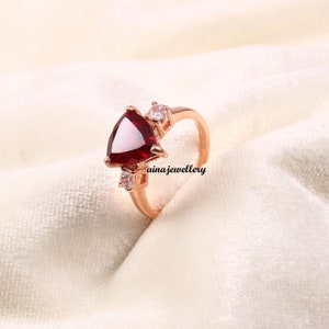 May include: A rose gold ring with a large, triangular, red gemstone and three smaller, round, white gemstones.