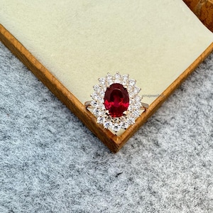May include: A silver ring with a large oval-shaped red gemstone surrounded by a halo of smaller white gemstones.