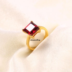 May include: A gold ring with a large, square, red gemstone.