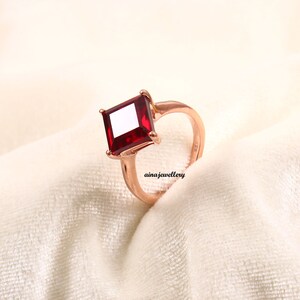 May include: A rose gold ring with a square-shaped red gemstone.