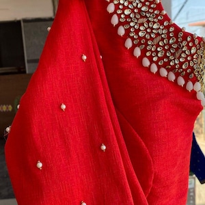 Könnte beinhalten: Rote Stoffbluse mit einem perlenbesetzten Ausschnitt. Der Ausschnitt ist mit weißen Perlen und klaren Strasssteinen verziert. Die Bluse hat ein schlichtes Design und ist perfekt für einen besonderen Anlass.