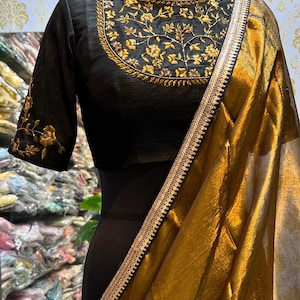 Puede incluir: Una blusa negra bordada con hilo dorado y lentejuelas, combinada con un sari dorado y negro con un borde dorado.