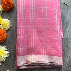 May include: A folded pink fabric textile featuring a white grid pattern and a metallic silver border along the bottom edge. The material displays a woven texture and is presented in a rectangular shape with clean, straight edges and folds.