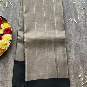 May include: A folded rectangular textile featuring a muted taupe-gray base with vertical white pinstripes. The fabric has a distinct horizontal border in solid black at the bottom edge, creating a sharp contrast against the neutral-toned main body.
