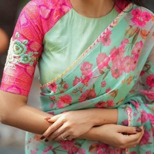 May include: A mint green blouse with pink floral sleeves and a matching floral patterned scarf. The sleeves have embroidered floral details. The scarf and sleeves have a pink and mint green floral pattern.