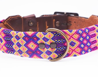 May include: A colorful dog collar with a geometric pattern in purple, pink, and yellow. The collar has a brown leather backing and a metal buckle and D-ring. The collar is approximately 1.5 inches wide.