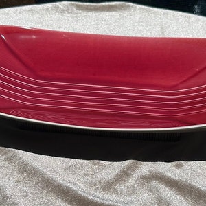 May include: A deep red ceramic serving bowl with a white rim and white lines on the inside. The bowl has a slightly curved shape.