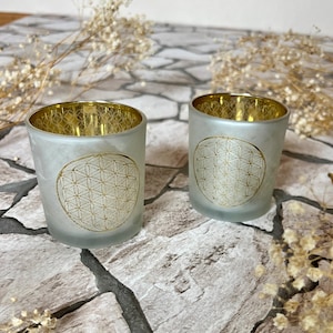 May include: Two frosted glass candle holders with a gold geometric design. The holders are on a stone surface.