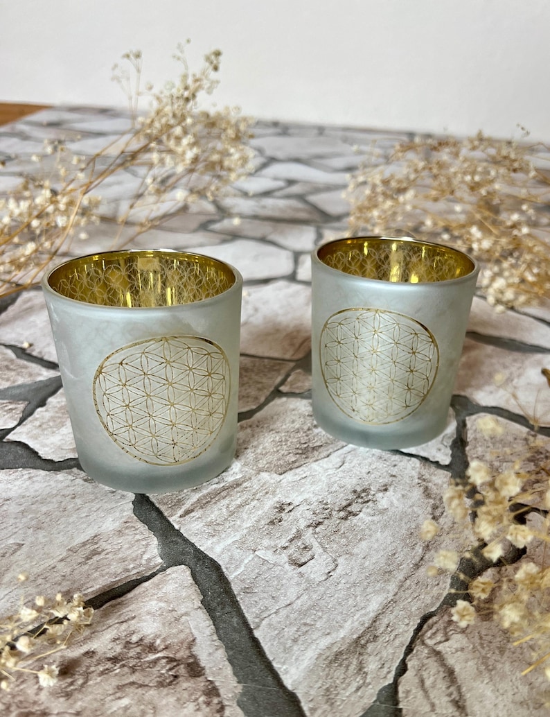 May include: Two frosted glass candle holders with a gold geometric design. The holders are on a stone surface.