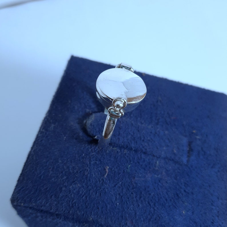 May include: A silver ring with a round, smooth top. The ring has a small, round detail on the side.