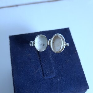 May include: A silver locket with a hinged lid, open to reveal an empty interior. The locket is on a blue velvet background.
