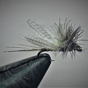 May include: A close-up of a fly fishing lure with a white and green body and a brown tail. The lure is tied to a hook and is held in a pair of pliers.
