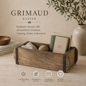 Könnte beinhalten: Eine rechteckige Holzkiste mit dunklen Metallbändern an den Seiten. Im Inneren befinden sich ein beigefarbenes Tuch, ein Garnknäuel und zwei Bücher, von denen eines mit Simple Things betitelt ist. Der Text Grimaud Kasten ist über der Kiste zu sehen.