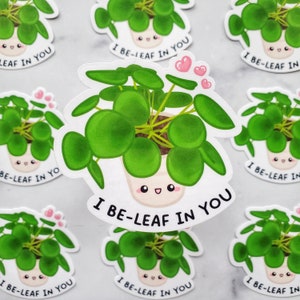 May include: A set of stickers featuring a cartoon illustration of a potted plant with the text "I be-leaf in you". The plant has round, green leaves and a smiling face.