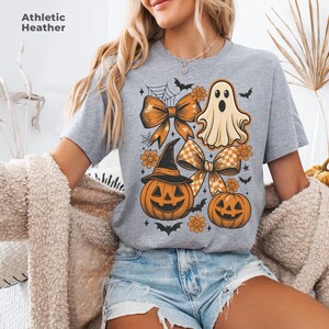 Pode incluir: Camiseta cinza Athletic Heather com um design de Halloween. O design inclui la&ccedil;os laranja, ab&oacute;boras, um fantasma, morcegos e flores. O texto "Athletic Heather" &eacute; impresso no canto superior esquerdo.