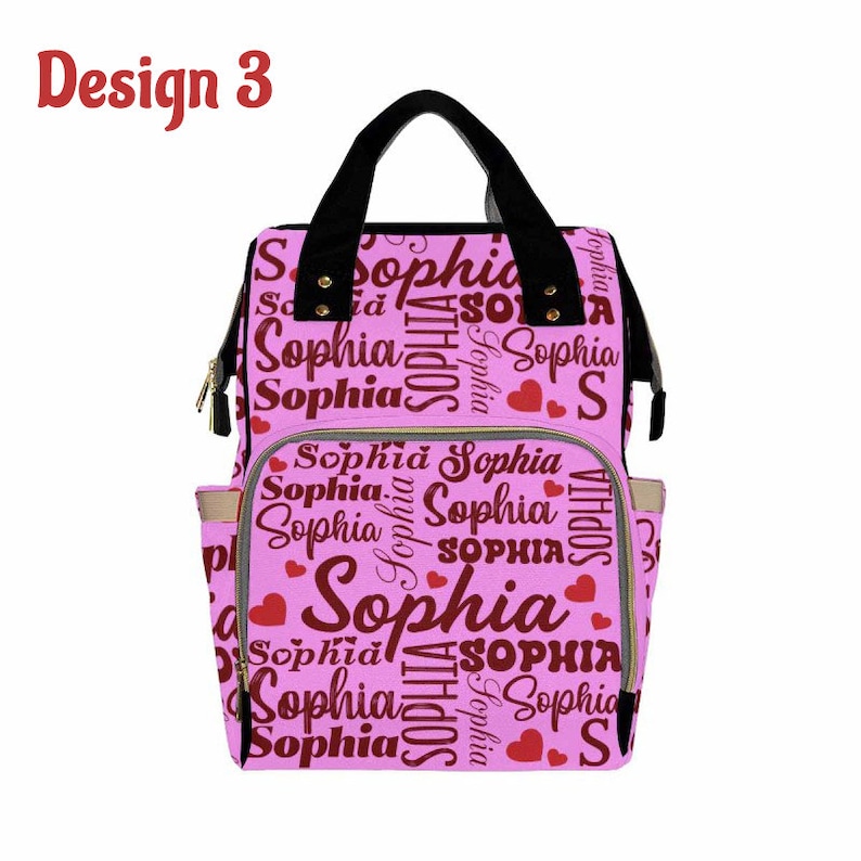 K&ouml;nnte beinhalten: Rosa Wickeltasche mit schwarzen Tr&auml;gern und goldenen Akzenten. Die Tasche ist mit einem sich wiederholenden Muster des Namens "Sophia" in burgunderfarbener Schrift mit roten Herzen bedeckt.