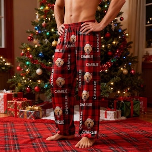 May include: Red plaid pajama pants with a repeating pattern of a golden retriever wearing a Santa hat and the name "Charlie". The pants are displayed in front of a Christmas tree.