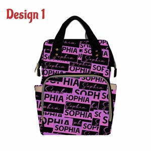 K&ouml;nnte beinhalten: Eine schwarze und lila Wickeltasche mit dem Namen "Sophia", der sich in einem Muster auf der Vorderseite wiederholt. Die Tasche hat eine Rei&szlig;verschlusstasche auf der Vorderseite und zwei Seitentaschen.