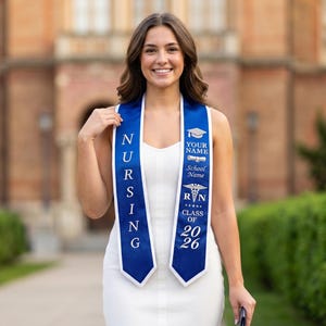 Op de afbeelding: Een blauwe en witte afstudeer-sjerp met het woord "NURSING" verticaal in het wit gedrukt. De sjerp heeft ook een afstudeerhoed, diploma, RN-symbool en de tekst "CLASS OF 2026".