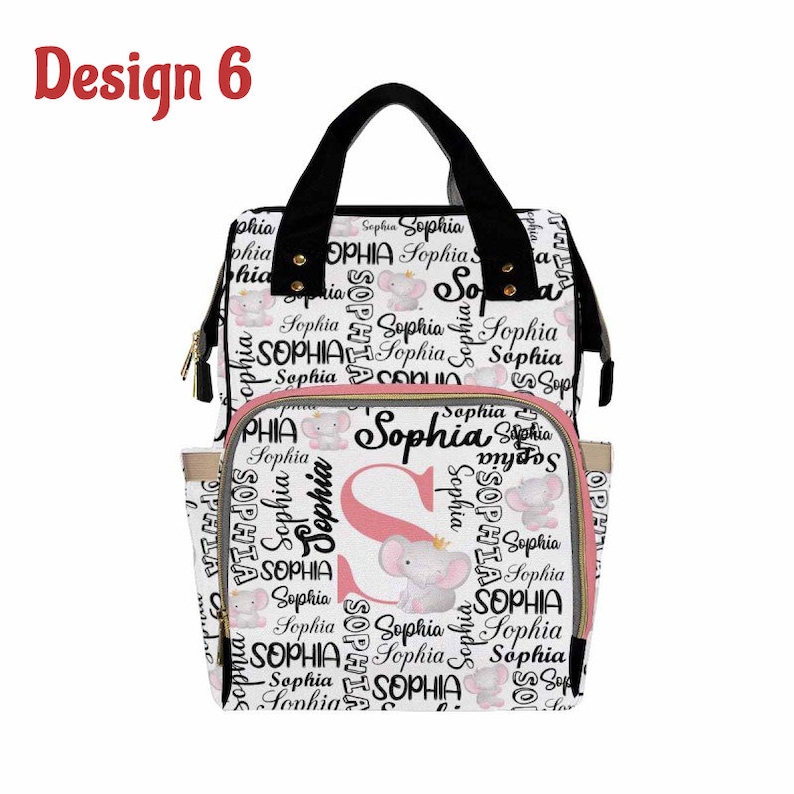 K&ouml;nnte beinhalten: Wei&szlig;e Wickeltasche mit einem rosa und schwarzen Muster mit dem Namen "Sophia" und einem kleinen Elefanten-Design. Die Tasche hat einen schwarzen Griff und verstellbare Tr&auml;ger.