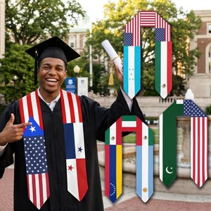 Könnte beinhalten: Ein lächelnder Absolvent in schwarzer Robe und Hut zeigt auf eine Abschluss-Schärpe mit dem Design der amerikanischen Flagge. Andere Schärpen zeigen Flaggen verschiedener Länder. Der Absolvent hält ein Diplom mit einer goldenen Quaste.