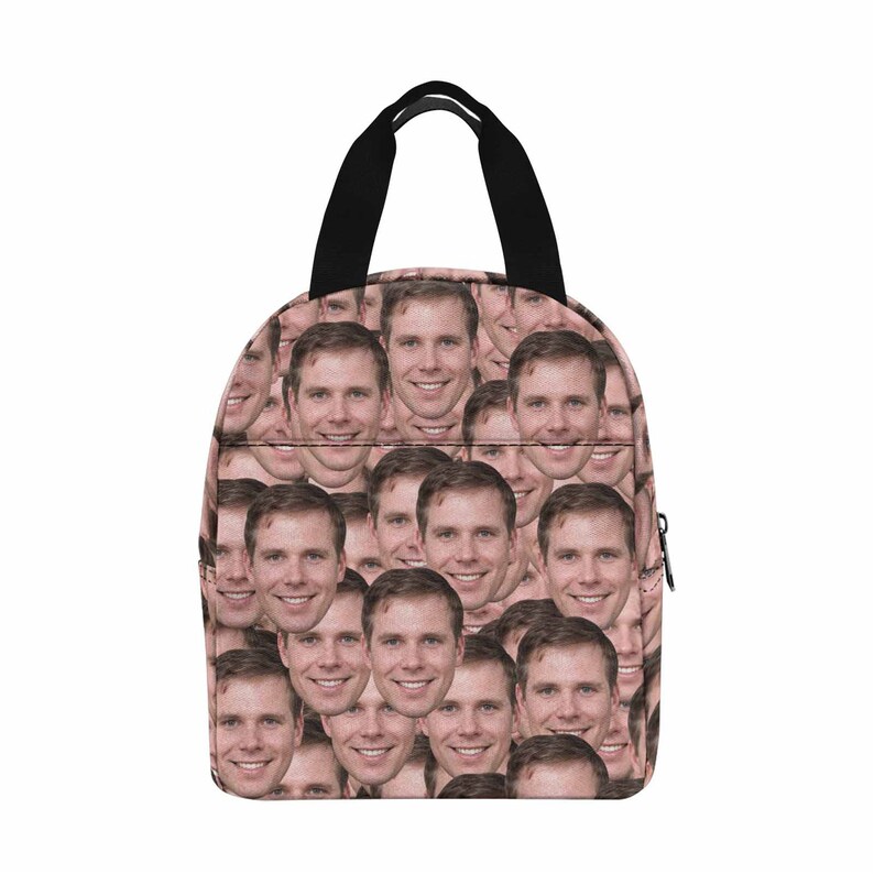 May include: A pink lunch bag with a black handle and zipper. The bag is covered in a repeating pattern of a man's face.