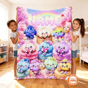 May include: A rectangular fleece blanket featuring a colorful, whimsical illustration of various smiling dumpling characters with faces, sitting on stacks of macarons. The word NAME is printed in large, bubble-style letters at the top center.