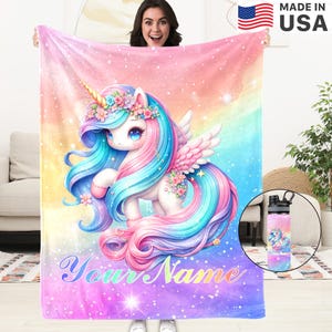 Peut inclure: Une couverture colorée avec une licorne de dessin animé, ornée d'une corne dorée, d'une couronne florale et d'une crinière et d'une queue bleues, roses et turquoise. La couverture a un fond arc-en-ciel et le texte "Your Name". Une gourde assortie est également visible.
