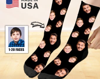 Könnte beinhalten: Schwarze Socken mit mehreren aufgedruckten Gesichtern. Die Socken haben ein "Made in USA"-Etikett und ein Foto eines jungen Jungen. Der Text "1-20 FACES" ist ebenfalls sichtbar. Die Socken befinden sich auf einer Holzoberfläche.
