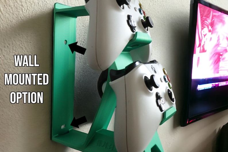 K&ouml;nnte beinhalten: Ein wandmontierter, t&uuml;rkisfarbener, 3D-gedruckter St&auml;nder f&uuml;r zwei wei&szlig;e Videospiel-Controller. Der St&auml;nder hat ein Loch zum Anbringen an einer Wand.