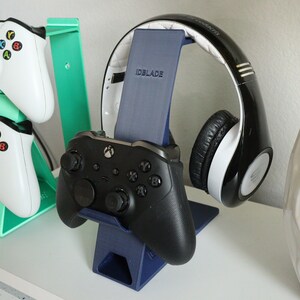 K&ouml;nnte beinhalten: Ein blauer und gr&uuml;ner 3D-gedruckter St&auml;nder h&auml;lt zwei wei&szlig;e Xbox-Controller. Ein separater blauer St&auml;nder h&auml;lt ein schwarz-wei&szlig;es Headset mit dem Text "IDBLADE" auf dem St&auml;nder.