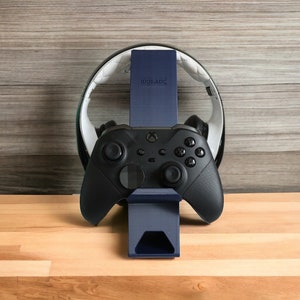 K&ouml;nnte beinhalten: Ein schwarzer Gaming-Controller mit einem blauen St&auml;nder und einem wei&szlig;en Headset-St&auml;nder. Der St&auml;nder tr&auml;gt die Aufschrift "IDOLADE".