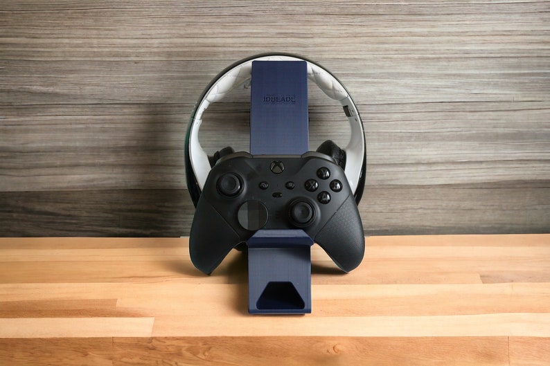 K&ouml;nnte beinhalten: Ein schwarzer Gaming-Controller mit einem blauen St&auml;nder und einem wei&szlig;en Headset-St&auml;nder. Der St&auml;nder tr&auml;gt die Aufschrift "IDOLADE".