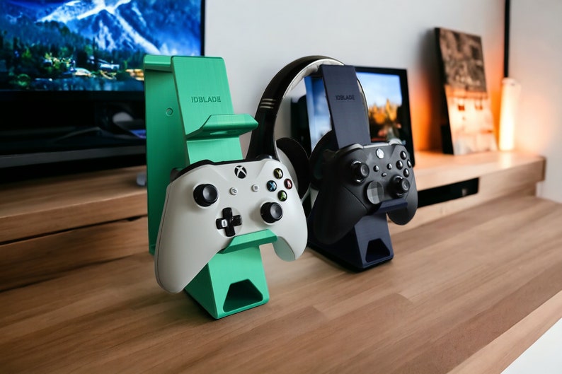 K&ouml;nnte beinhalten: Zwei Gaming-Controller-St&auml;nder, einer gr&uuml;n und einer schwarz, mit Controllern und einem Headset oben drauf. Die St&auml;nder sind mit "IDBLADE" beschriftet.
