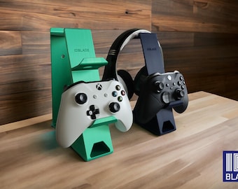 May include: A mint green and a navy blue gaming stand, each featuring the text IDBLADE. The mint stand holds a white game controller, while the navy stand holds a black game controller and a pair of black and white over-ear headphones.