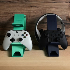 K&ouml;nnte beinhalten: Zwei Controller-St&auml;nder, einer gr&uuml;n und einer schwarz, mit Controllern darauf. Der gr&uuml;ne St&auml;nder hat den Text "IDBLADE" darauf. Der schwarze St&auml;nder hat den Text "Hyperkin" darauf.