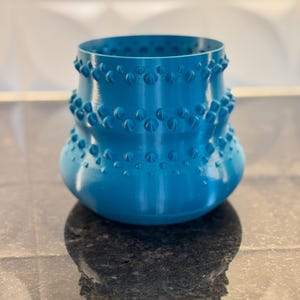 Può includere: Un vaso in ceramica blu turchese con un design testurizzato in rilievo. Il vaso ha una base larga e un collo stretto.