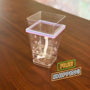 May include: A clear plastic plant pot with a square shape and a light purple and white rim. A white rope extends from the bottom of the pot. The words "FREE SHIPPING" are in a green and yellow box.