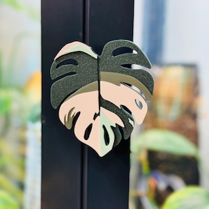 Op de afbeelding: Een groene en roze monstera-bladvormige deurknop.